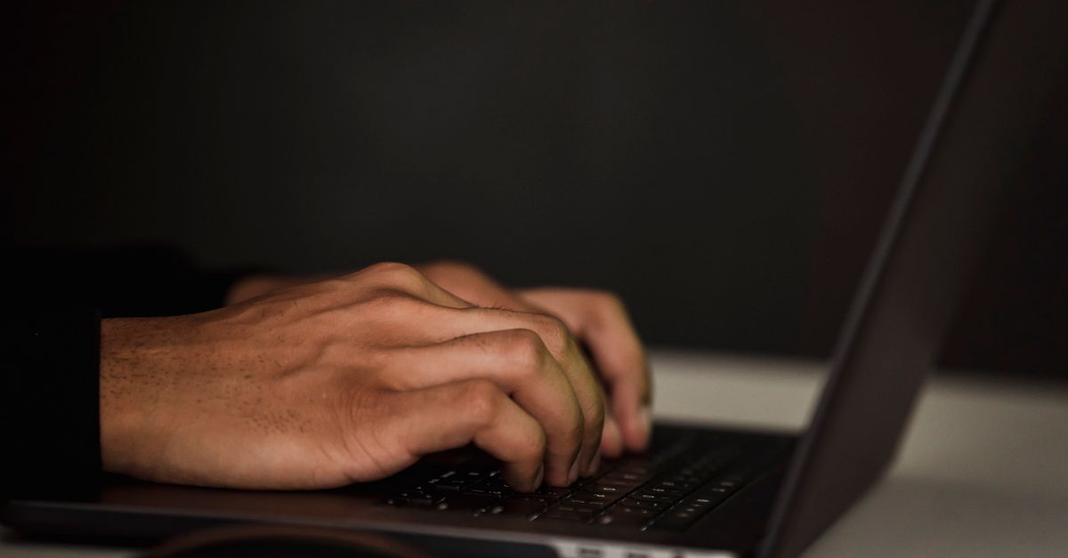 Manos tecleando en un portátil en un espacio de trabajo oscuro